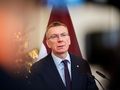 Na zdjęciu mężczyzna w garniturze z okularami, stojący przed flagą, wygląda na zmartwionego.