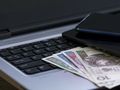 Na klawiaturze laptopa leży kilka banknotów oraz dwa telefony komórkowe.