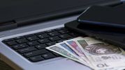 Na klawiaturze laptopa leży kilka banknotów oraz dwa telefony komórkowe.