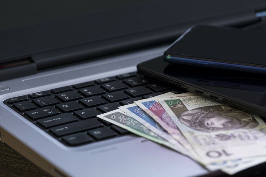 Na klawiaturze laptopa leży kilka banknotów oraz dwa telefony komórkowe.