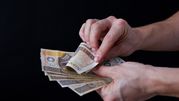 Zdjęcie rąk trzymających polskie banknoty na czarnym tle.