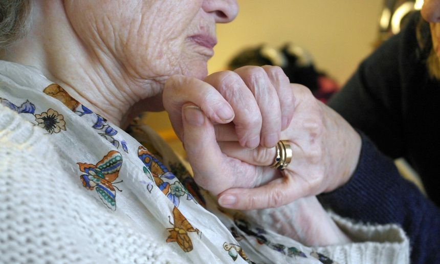 Dwie dłonie trzymają się nawzajem. W tle widać fragmenty odzieży i miękkie światło.