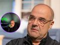 Cezary Żak w czarnej bluzie, słucha rozmowy w podcaście. Ujęcie twarzy i mikrofonu.