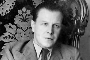 Mężczyzna w eleganckim garniturze na tle ozdobnej tapety. Wyraz twarzy poważny.