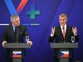 Dwaj mężczyźni przy mównicach, mówi jeden, drugi słucha; tło w kolorach niebieskim i zielonym.