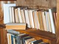 Zdjęcie półki z książkami w drewnianej bibliotece. Książki różnią się kolorami i rozmiarami.