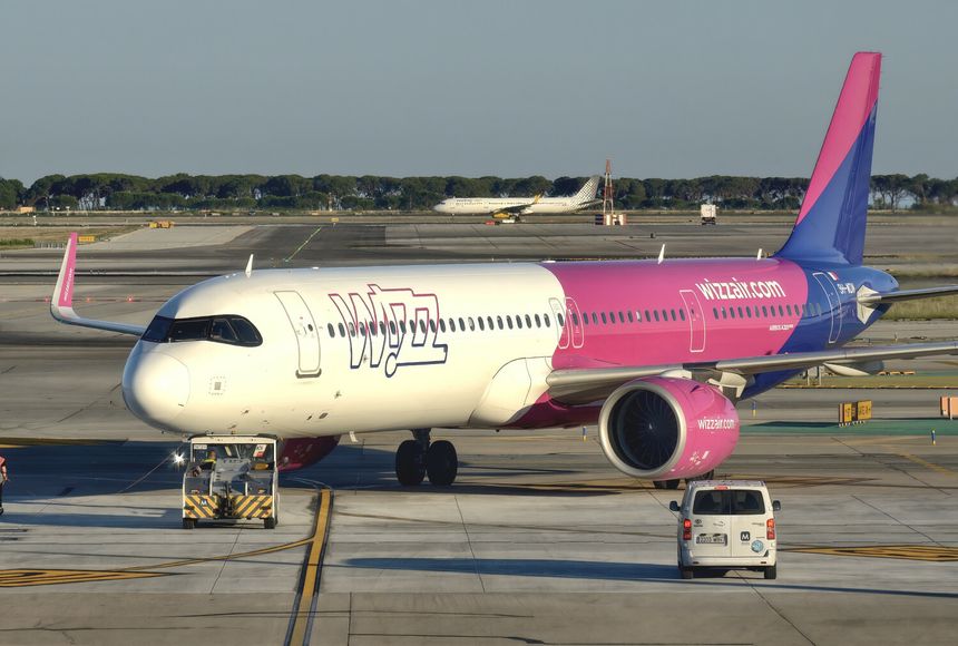 Samolot linii Wizz Air z różowym ogonem stoi na lotnisku przy ruchliwej płycie.