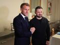 Na zdjęciu dwaj mężczyźni uśmiechają się i podają sobie ręce. W tle stonowane wnętrze.