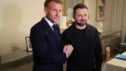 Na zdjęciu dwaj mężczyźni uśmiechają się i podają sobie ręce. W tle stonowane wnętrze.