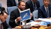 Mężczyzna w garniturze trzyma zdjęcie samolotu w trakcie dyskusji w ONZ. Obok inni delegaci.