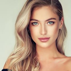 Kobieta z długimi, blond włosami i jasnymi oczami, patrzy w obiektyw z uśmiechem.