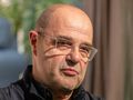 Cezary Żak z okularami, krótko ostrzyżony, w ciemnym ubraniu, z wyrazem zamyślenia.