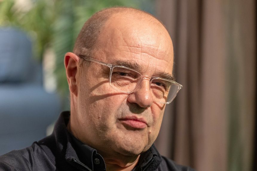Cezary Żak z okularami, krótko ostrzyżony, w ciemnym ubraniu, z wyrazem zamyślenia.