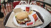 Na tacy znajduje się hamburger z sezamową bułką, frytki i napój, w tle stół w McDonald's.