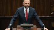Na zdjęciu mężczyzna w ciemnym garniturze z czerwonym krawatem w parlamencie.