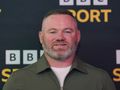 Na zdjęciu Wayne Rooney z brodą w zielonej koszuli, uśmiecha się na tle czarno-żółtym.