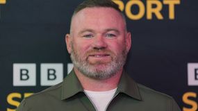 Na zdjęciu Wayne Rooney z brodą w zielonej koszuli, uśmiecha się na tle czarno-żółtym.