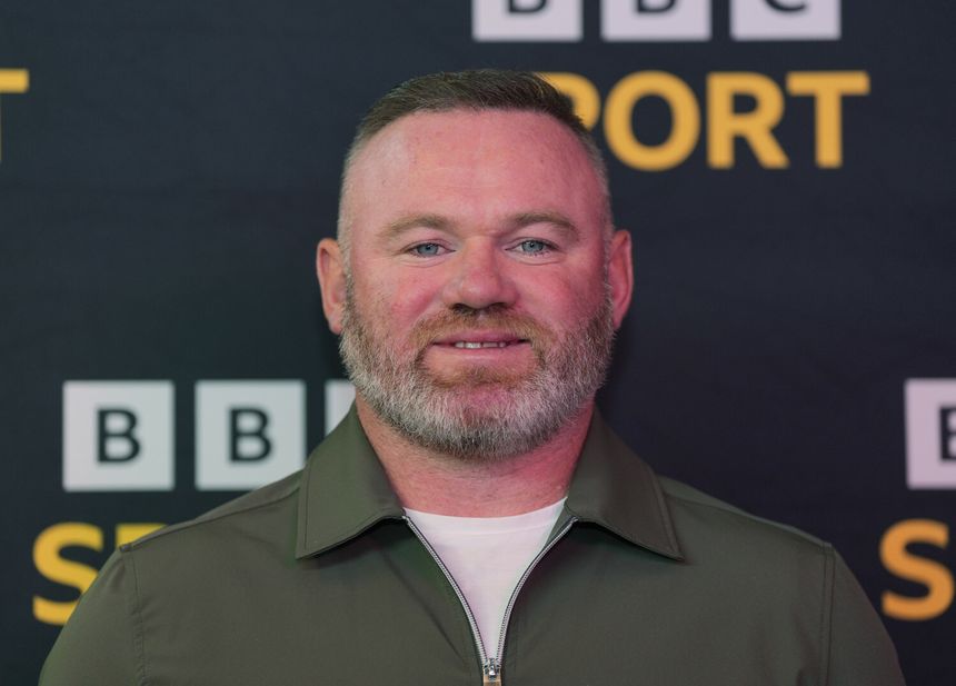 Na zdjęciu Wayne Rooney z brodą w zielonej koszuli, uśmiecha się na tle czarno-żółtym.