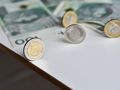 Na stole leżą monety i banknoty polskich złotych. Widoczna moneta 5 zł.