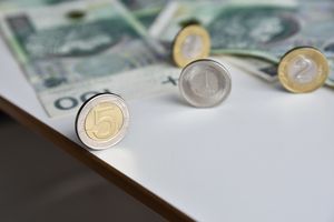 Na stole leżą monety i banknoty polskich złotych. Widoczna moneta 5 zł.