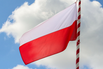 Flaga Polski powiewająca na maszcie, w tle niebo z białymi chmurami.