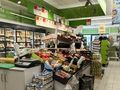 Widok wnętrza sklepu spożywczego z warzywami, owocami i lodówkami wypełnionymi produktami.