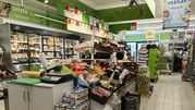 Widok wnętrza sklepu spożywczego z warzywami, owocami i lodówkami wypełnionymi produktami.