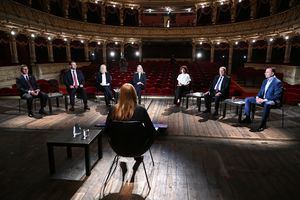 Dyskusja polityczna w teatrze, siedem osób w eleganckich ubraniach, widownia pusta.