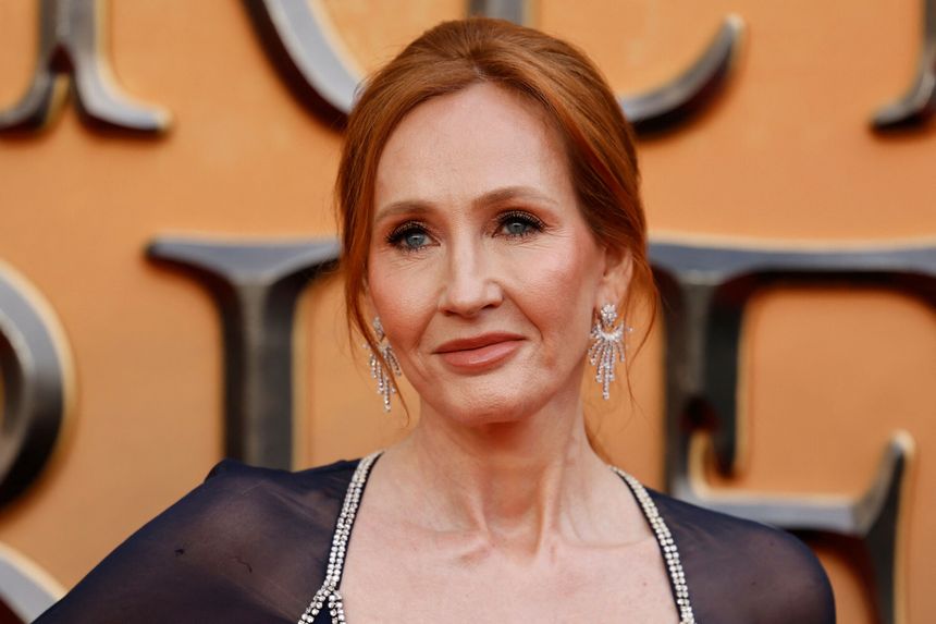 J.K. Rowling. Na zdjęciu uśmiechnięta kobieta z rudymi włosami, w eleganckiej sukni i dużych, błyszczących kolczykach.