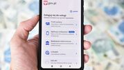 Smartfon w dłoni z ekranem logowania do usług e-administracji w Polsce. Tło to pieniądze.