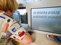 Osoba o krótkich włosach podchodzi do okienka z wyświetlaczem z napisem.