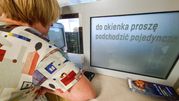 Osoba o krótkich włosach podchodzi do okienka z wyświetlaczem z napisem.