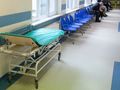 Wnętrze szpitala z wózkiem medycznym i niebieskimi krzesłami w poczekalni.