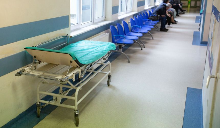 Wnętrze szpitala z wózkiem medycznym i niebieskimi krzesłami w poczekalni.