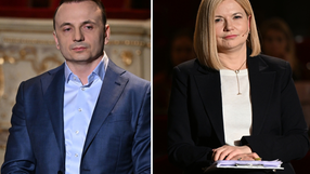 Dwoje ludzi w eleganckich strojach siedzi obok siebie, w tle widać zarys sceny.