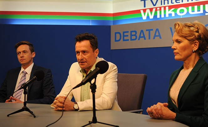 Na zdjęciu trzech polityków podczas debaty, siedzących za mikrofonami w studiu telewizyjnym.