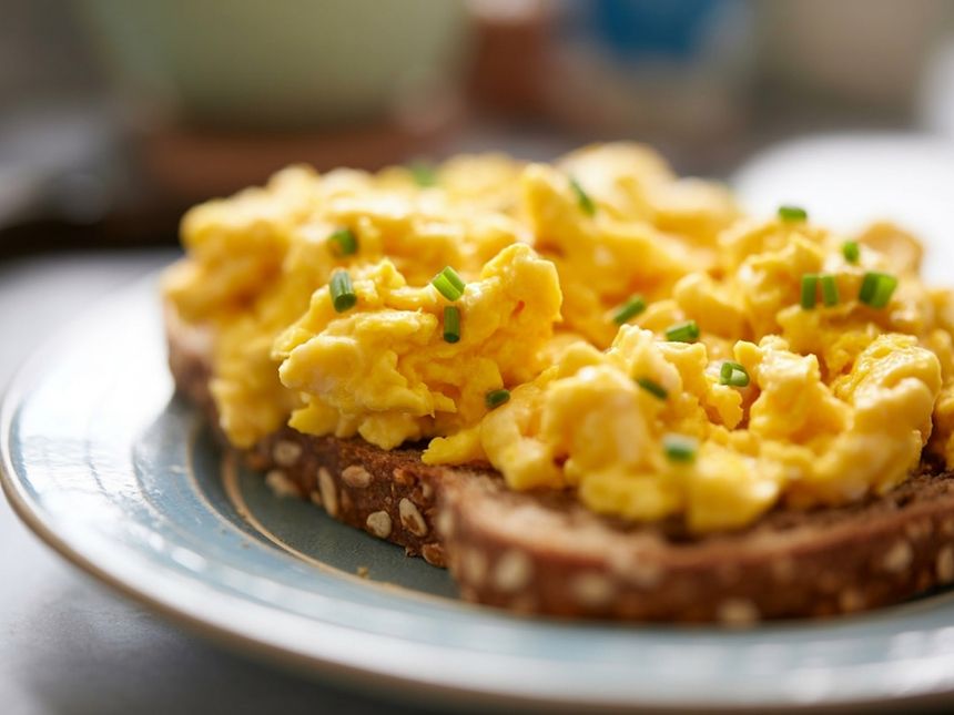 Tost z jajecznicą posypany szczypiorkiem, na talerzu z wzorem.