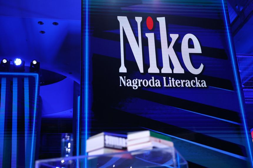 Na zdjęciu logo nagrody literackiej Nike na niebieskim tle, z książkami w tle.