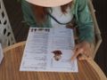 Kobieta w kapeluszu przegląda menu na stole w kawiarni, wskazując na danie palcem.