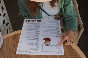 Kobieta w kapeluszu przegląda menu na stole w kawiarni, wskazując na danie palcem.