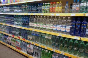 Półka z różnymi rodzajami butelek wody mineralnej i smakowej, uporządkowane w rzędach.