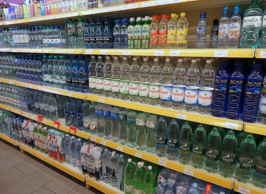 Półka z różnymi rodzajami butelek wody mineralnej i smakowej, uporządkowane w rzędach.