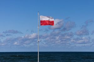 Flaga Polski na tle nieba i morza, w otoczeniu białych chmur.
