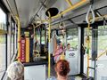 Wnętrze autobusu miejskiego z pasażerami siedzącymi i stojącymi, widoczny biletomat.