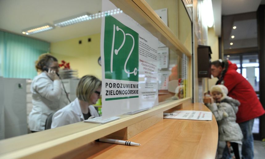 Pracownicy przy biurku w przychodni, w tle dzieci i pacjentka na telefonie. Plakat z logo Zielonogórskiego.