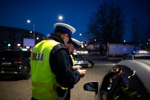 Dwa policjanty w żółtych kamizelkach kontrolują kierowcę przy samochodzie nocą.