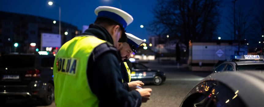 Dwa policjanty w żółtych kamizelkach kontrolują kierowcę przy samochodzie nocą.