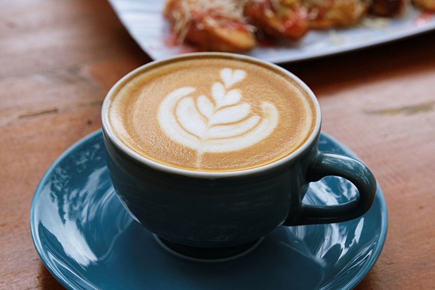 Kawa latte w niebieskiej filiżance z wzorem na mlecznej piance. Tło drewniany stół.