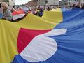 Tłum demonstrantów trzymających wielką flagę, z transparentami w dłoniach.