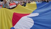 Tłum demonstrantów trzymających wielką flagę, z transparentami w dłoniach.